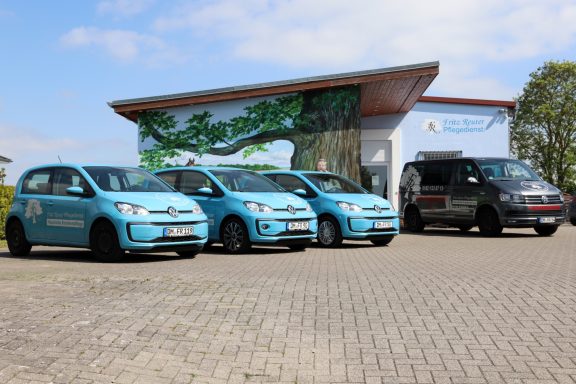 Fritz Reuter Pflegedienst GmbH Vier Autos, drei hellblau und ein dunkelgrau, stehen vor einem modernen Gebäude.
